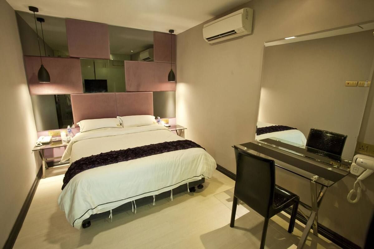 Habitación de hotel con cama, mesitas de noche, escritorio con silla, equipo de aire acondicionado y espejo.
