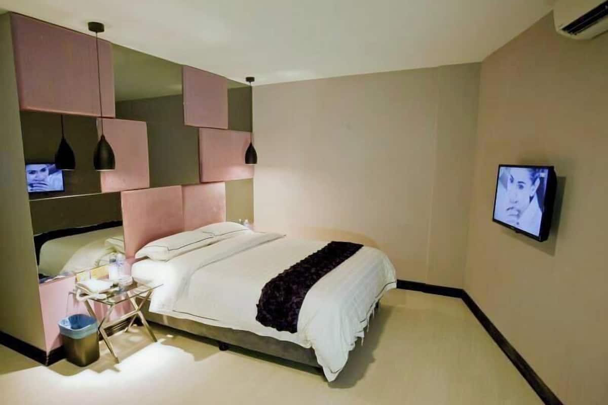 Una habitación de hotel con cama, mesita de noche, televisión y un cubo de basura.