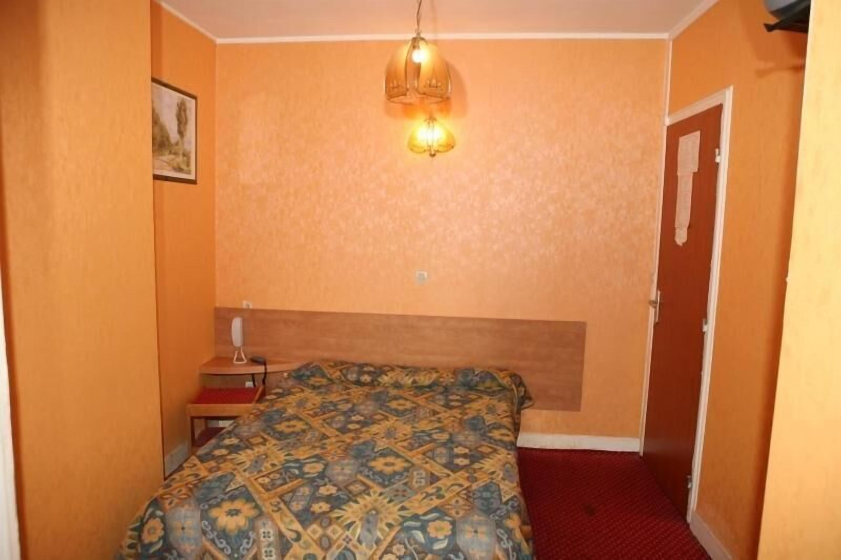 A bedroom with a patterned bedspread, a bedside table with a lamp, and a door.