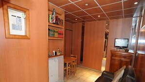 A cozy living area with a leather sofa, wooden shelves, a tiled floor, and a television. - Sully Hôtel (Paris)