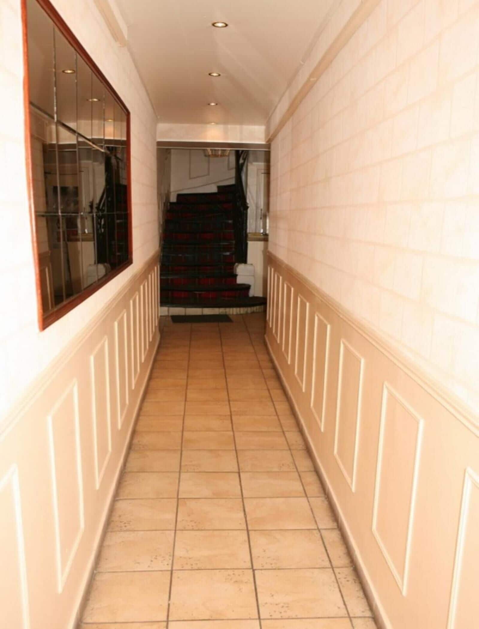 A narrow hallway with tiled flooring, white walls, and a wooden-framed window on the left.