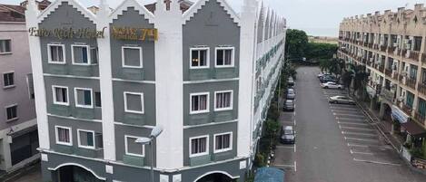 A multi-story hotel with a modern design, featuring balconies and a parking area.