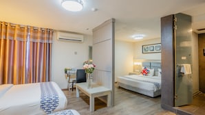 Une chambre d’hôtel avec deux lits, un bureau, une chaise, un vase de fleurs et une salle de bain dot ée d’une douche à paroi de verre.