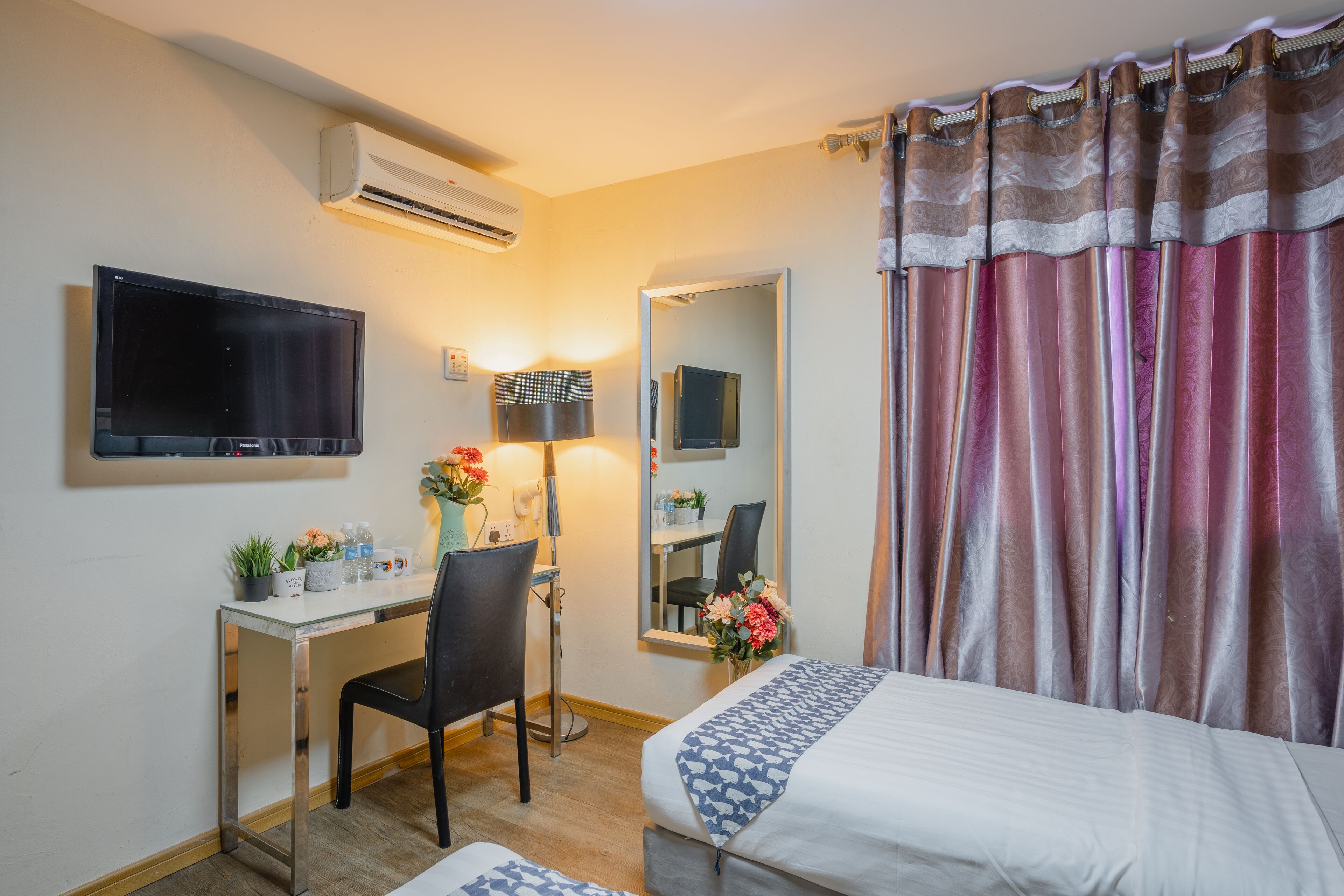 Habitación de hotel con cama, escritorio con silla, televisor de pantalla plana, aire acondicionado, espejo y ventana con cortinas.