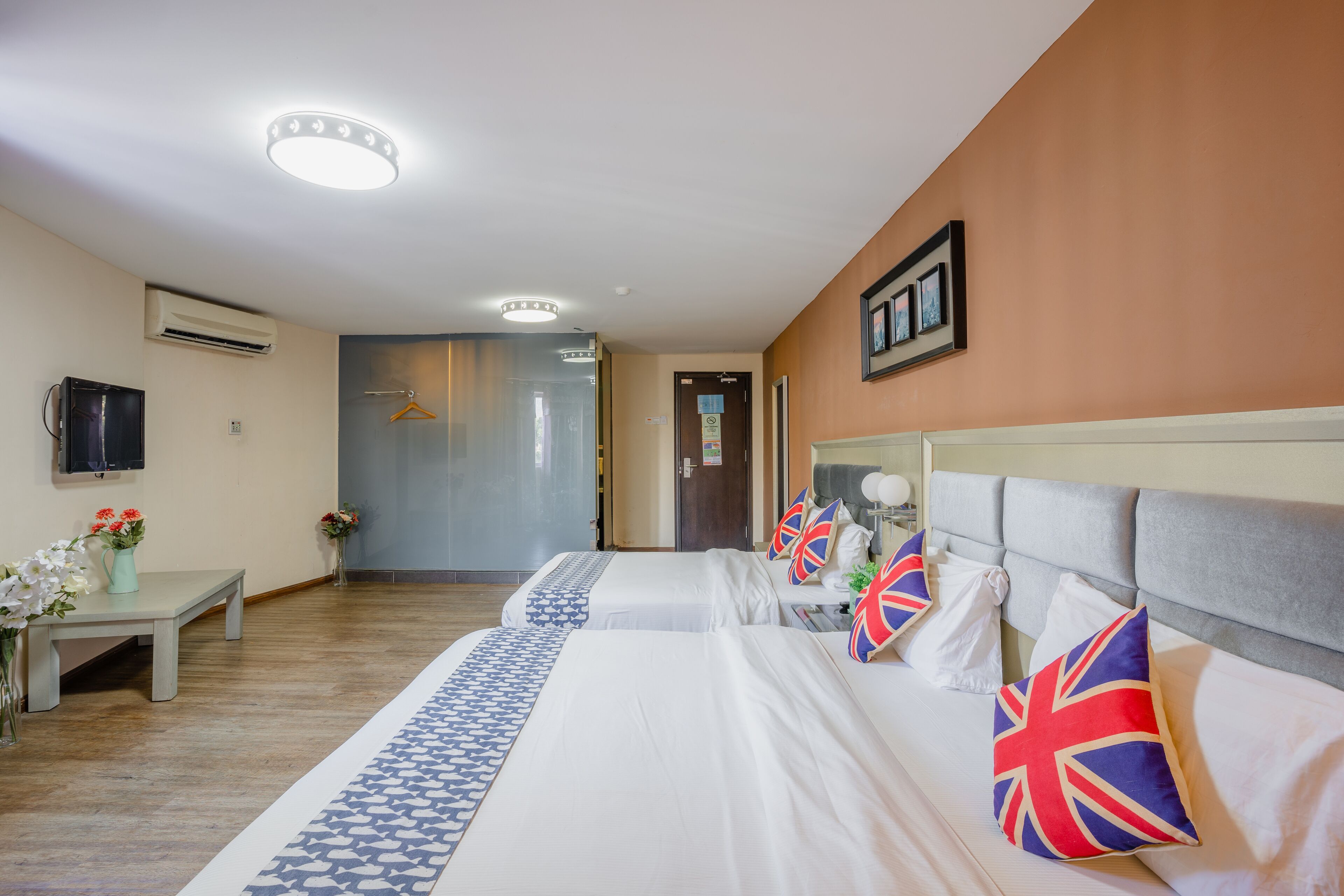 Habitación de hotel con dos camas, un televisor, un escritorio con un florero y una puerta que da a otra habitación.