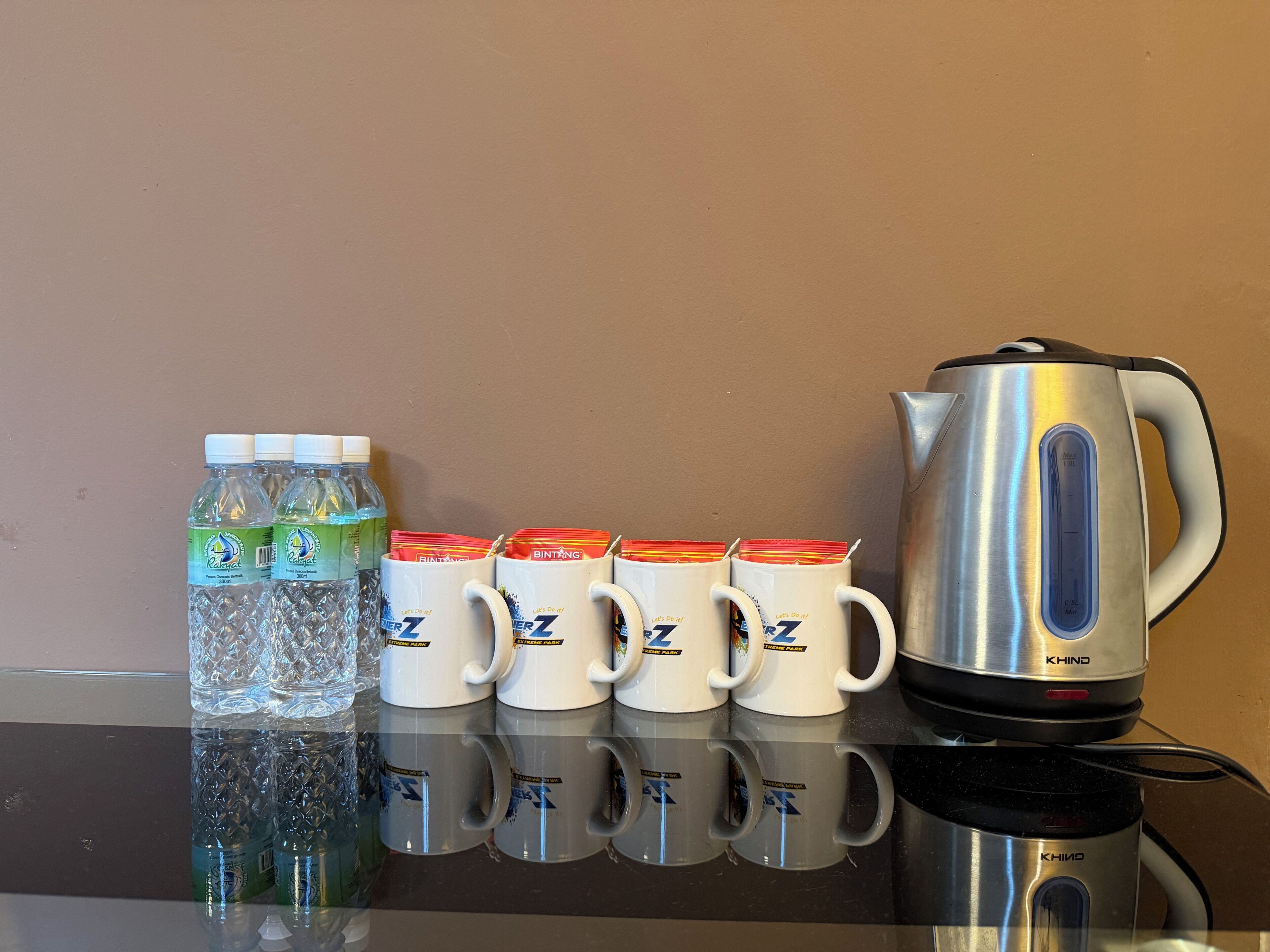 A stainless steel kettle, four water bottles, and six white mugs on a reflective surface.