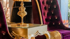 Une chambre luxueuse avec un canapé moelleux en velours violet, une lampe dorée et une statue équestre décorative.