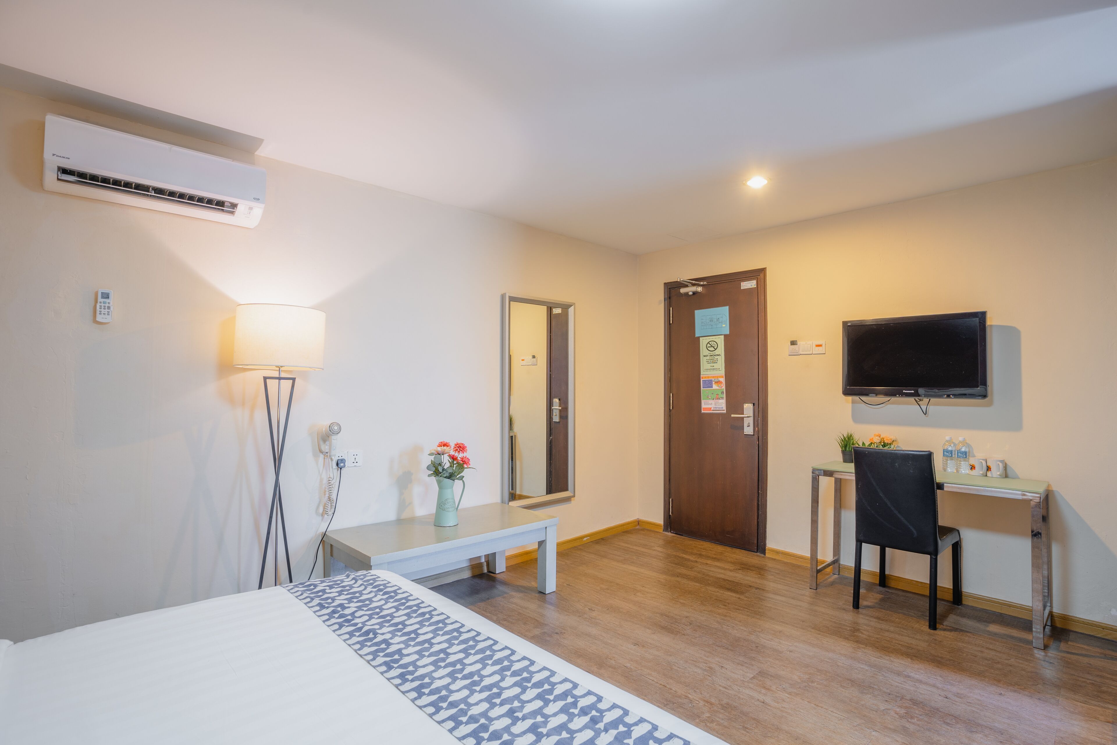 Habitación de hotel con cama, mesita de noche, lámpara, escritorio con silla, televisor y aire acondicionado.