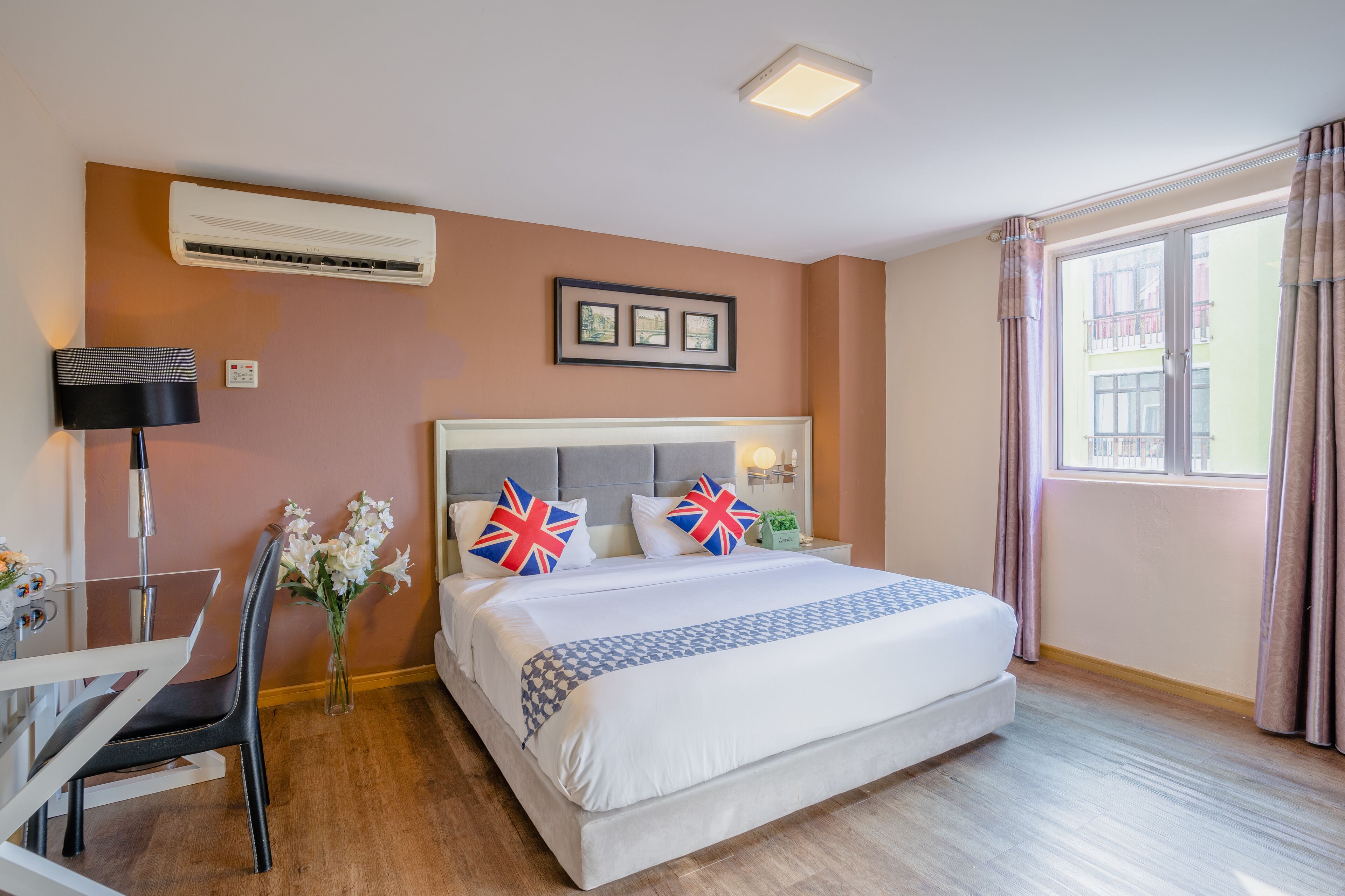 Ein Hotelzimmer mit einem großen Bett, einem Schreibtisch mit Stuhl, einer Klimaanlage, einem gerahmten Bild an der Wand und einem Fenster mit Vorhängen.