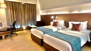 A hotel room with two beds, a desk, and a chair. - Regenta Central Grand Exotica Pune (Pune)