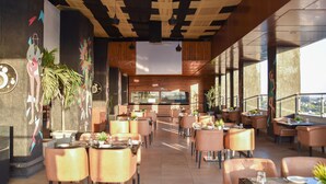 A modern restaurant with a central bar, multiple seating areas, and large windows providing views. - Regenta Central Grand Exotica Pune (Pune)