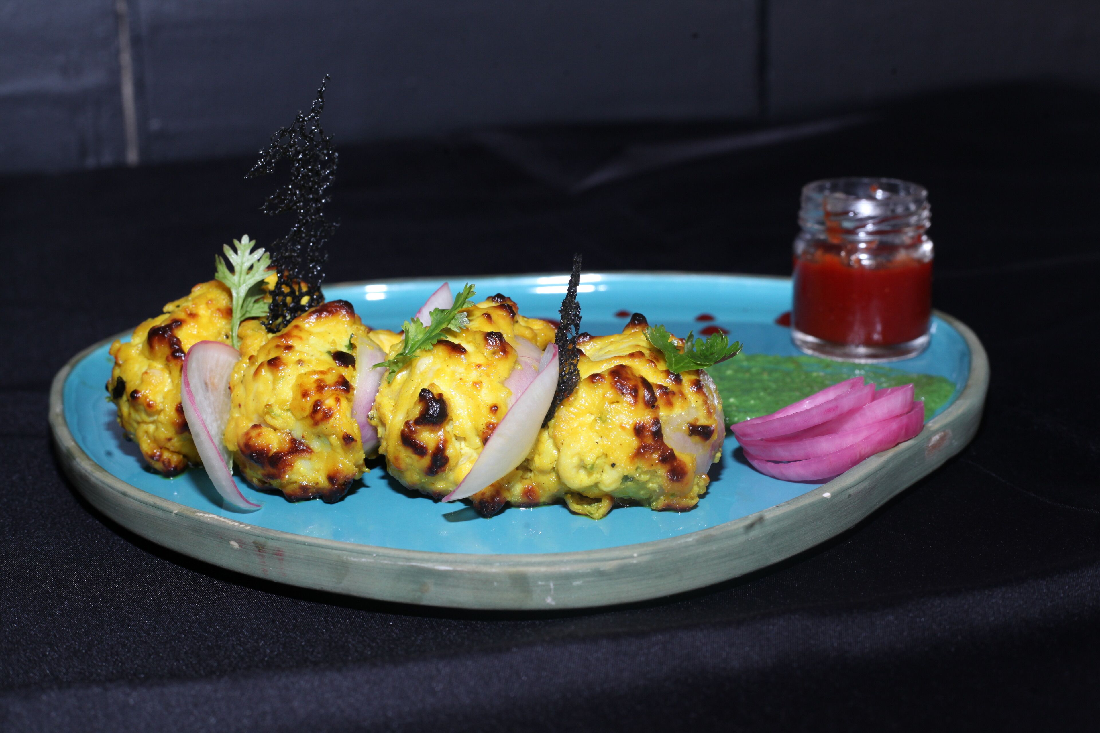 A plate of food with a blue rim, garnished with herbs and onions, and a small glass of sauce.