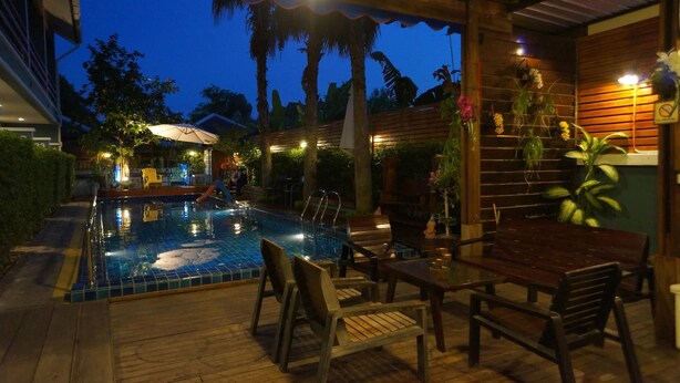 Zona de piscina exterior con mobiliario de cubierta de madera y piscina con baldosas.