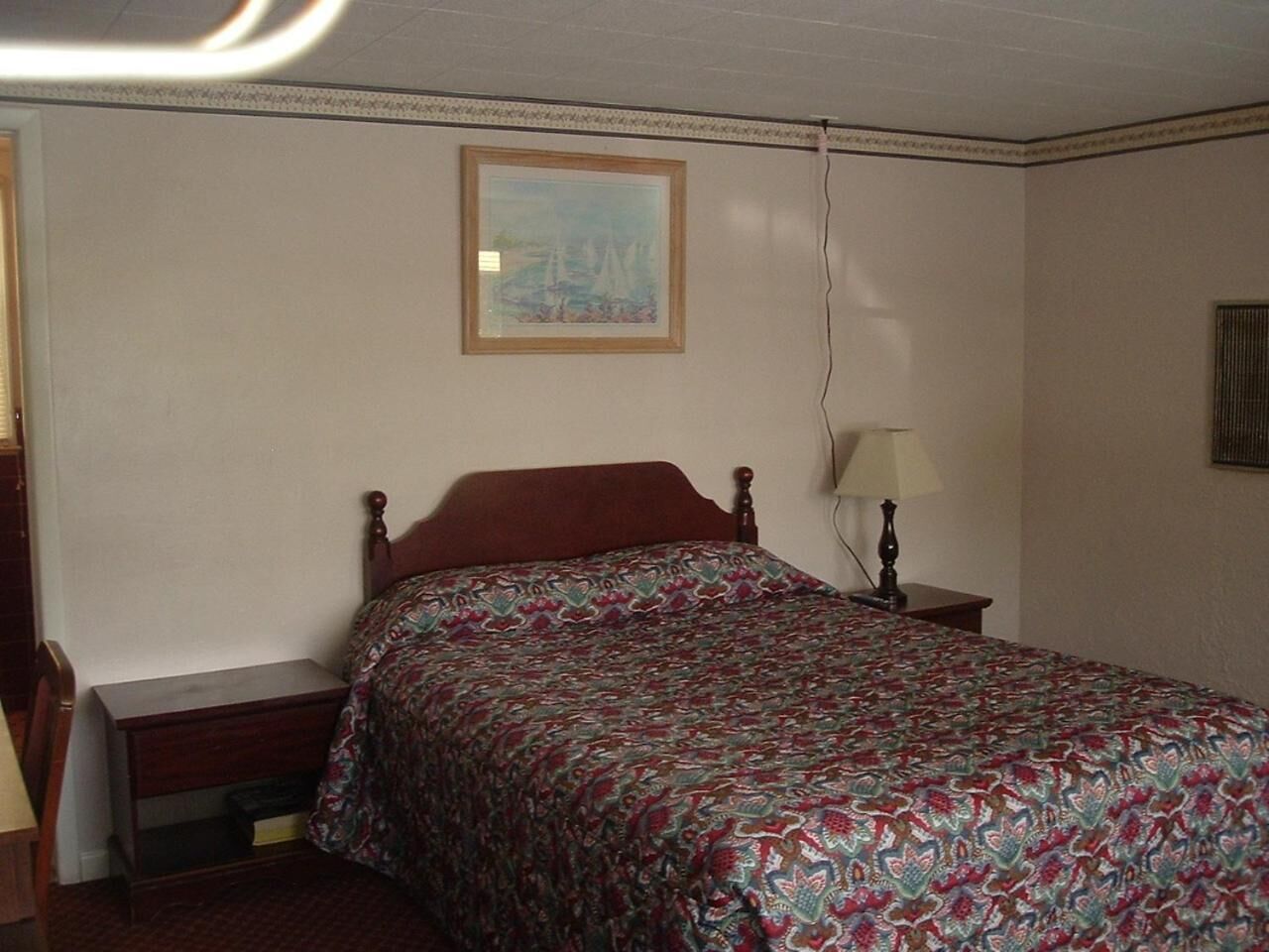 Une chambre à coucher avec un lit, une table de chevet, une lampe et un tableau au mur.