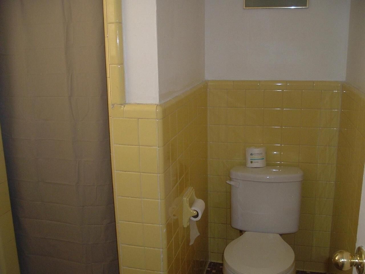 Un baño con paredes de azulejos amarillos, un inodoro blanco y un rollo de papel higiénico en la pared.