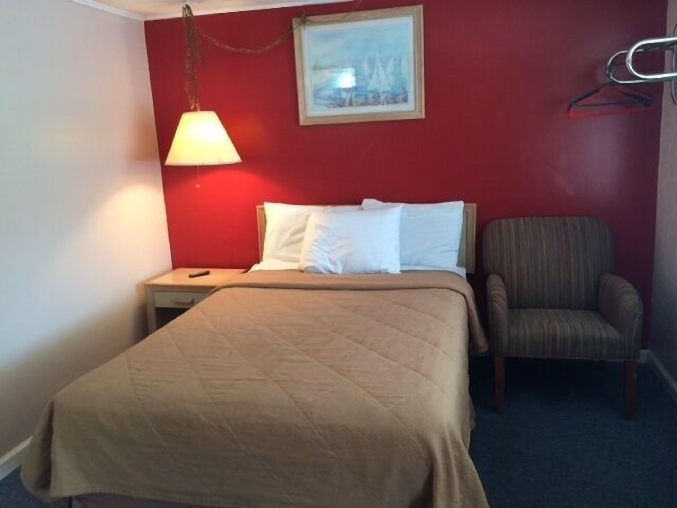 A hotel room with a bed, a chair, a nightstand, a lamp, and a painting on the wall.
