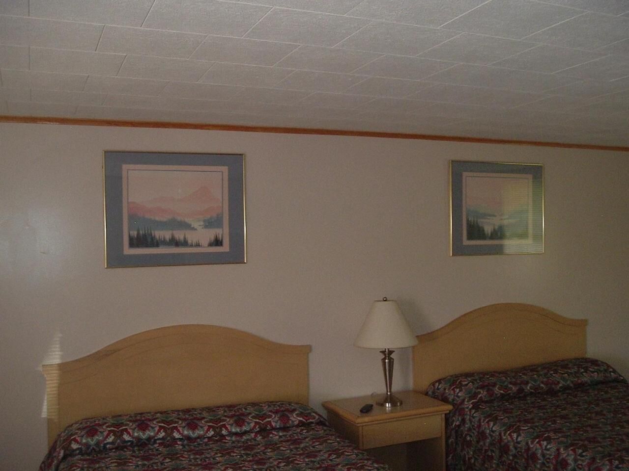 A hotel room with two beds, a nightstand with a lamp, and two framed pictures on the wall.