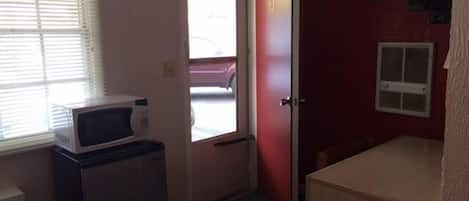 Ett litet rum med en mikrovågsugn på ett litet bord, en dörr med ett nummer och ett fönster med persienner.