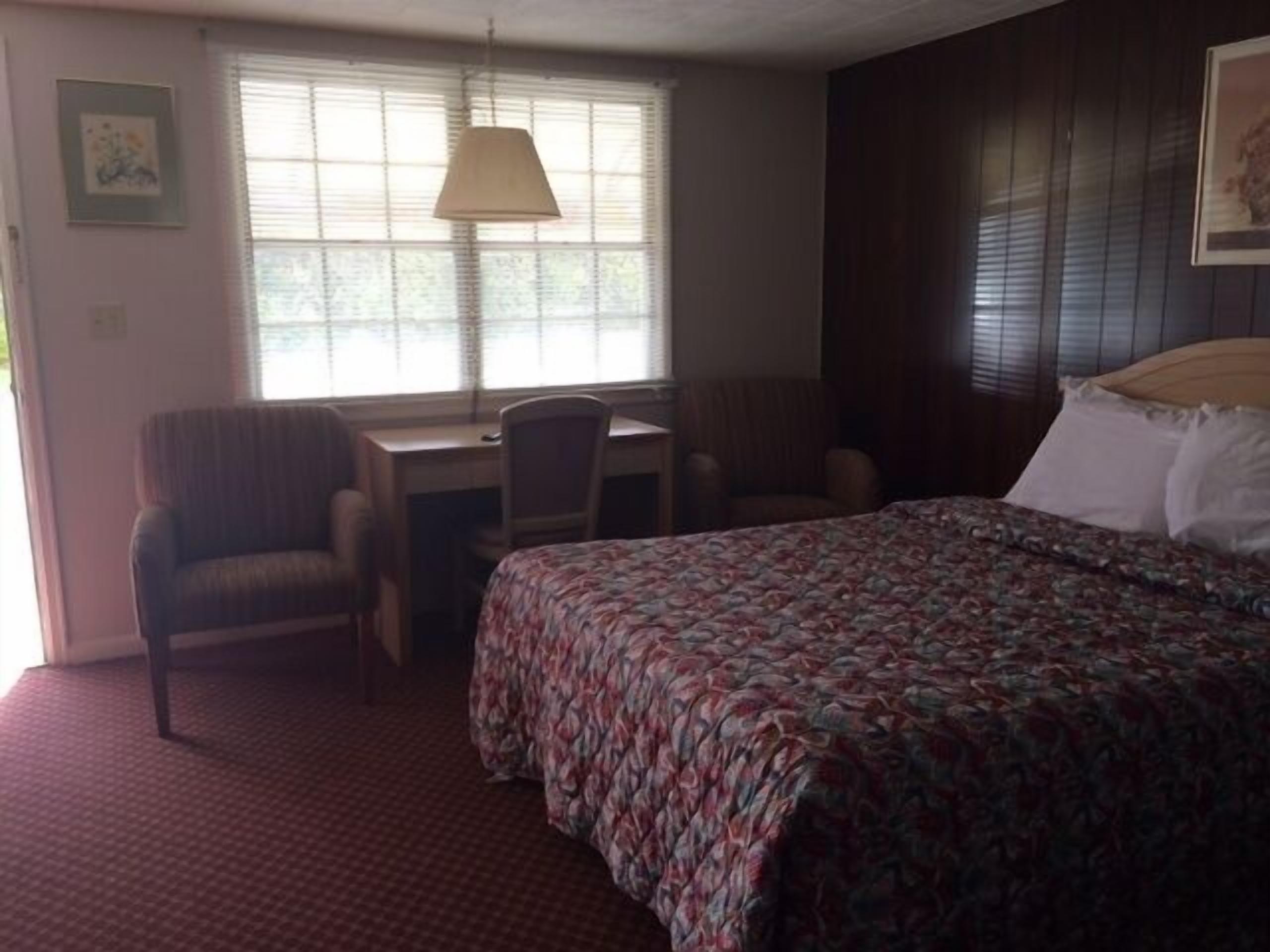 Une chambre d’hôtel avec un lit, un bureau, une chaise et une fenêtre avec des stores.