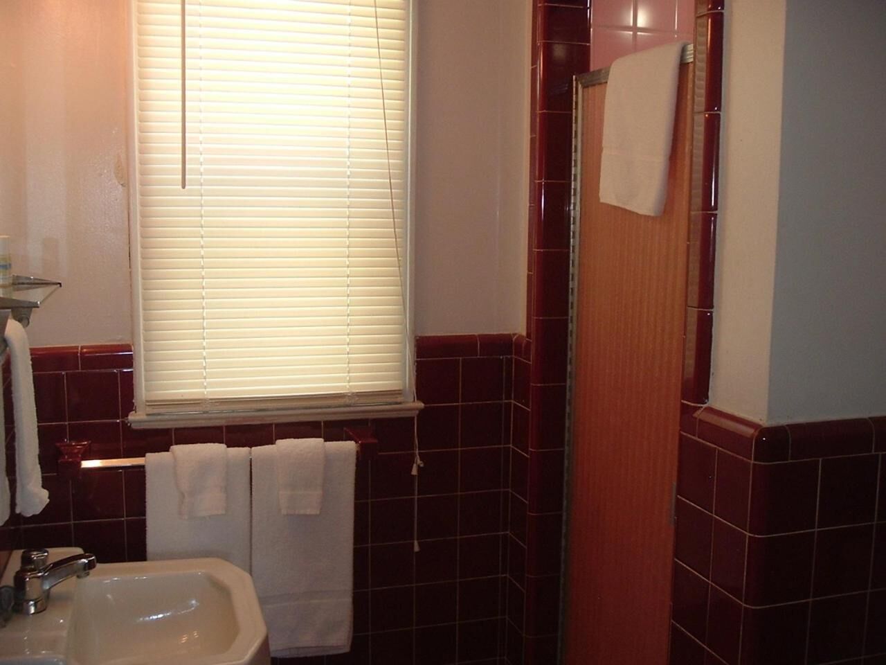 A bathroom with a sink, a window with blinds, and a shower area.