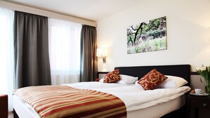 A hotel room with a large bed, a nightstand with a lamp, a painting on the wall, and a window with curtains. - City Stay Seefeld House (Zürich)