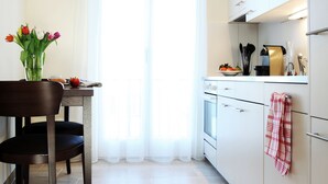 A modern kitchen with white cabinets, a dining table with chairs, and a vase of flowers. - City Stay Seefeld House (Zürich)