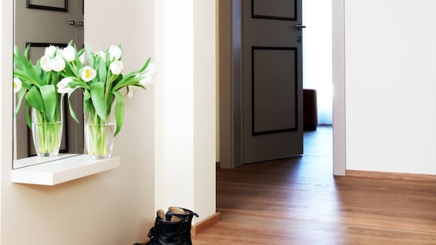 A hallway with a wooden floor, a pair of black boots, and a vase with white flowers on a shelf. - City Stay Seefeld House (Zürich)