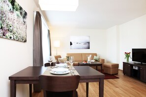 Una habitación de hotel moderna con zona de comedor, sofá, televisión y obras de arte en las paredes.
