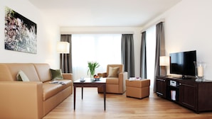 A modern living room with a sofa, armchair, coffee table, and a TV on a cabinet. - City Stay Seefeld House (Zürich)
