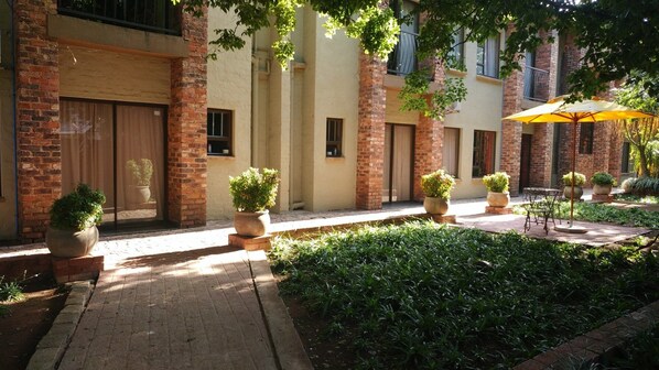 A courtyard with brick buildings, potted plants, and a table with an umbrella.