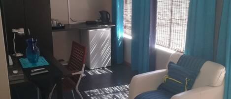 Un espacio habitable compacto con kitchenette, comedor y zona de estar con sofá y sillón.