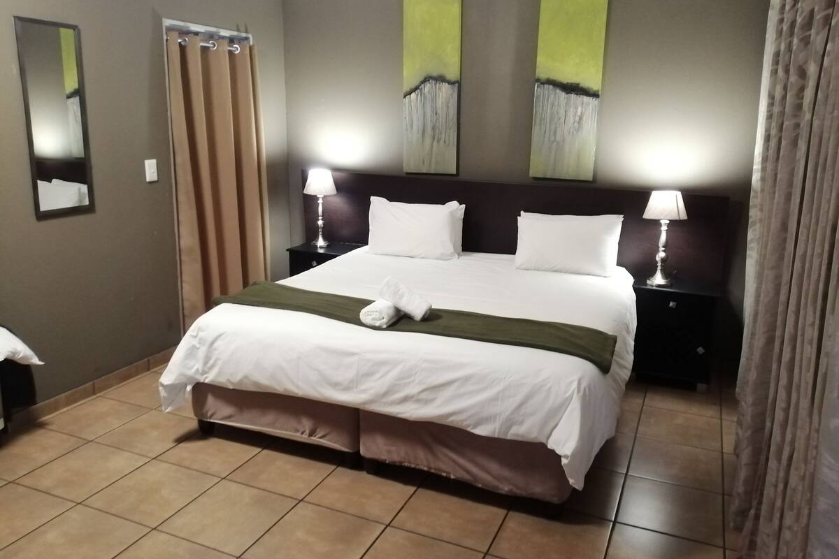 Ein Hotelzimmer mit einem großen Bett, zwei Nachttischen mit Lampen, einem Spiegel und Bildern an den Wänden.