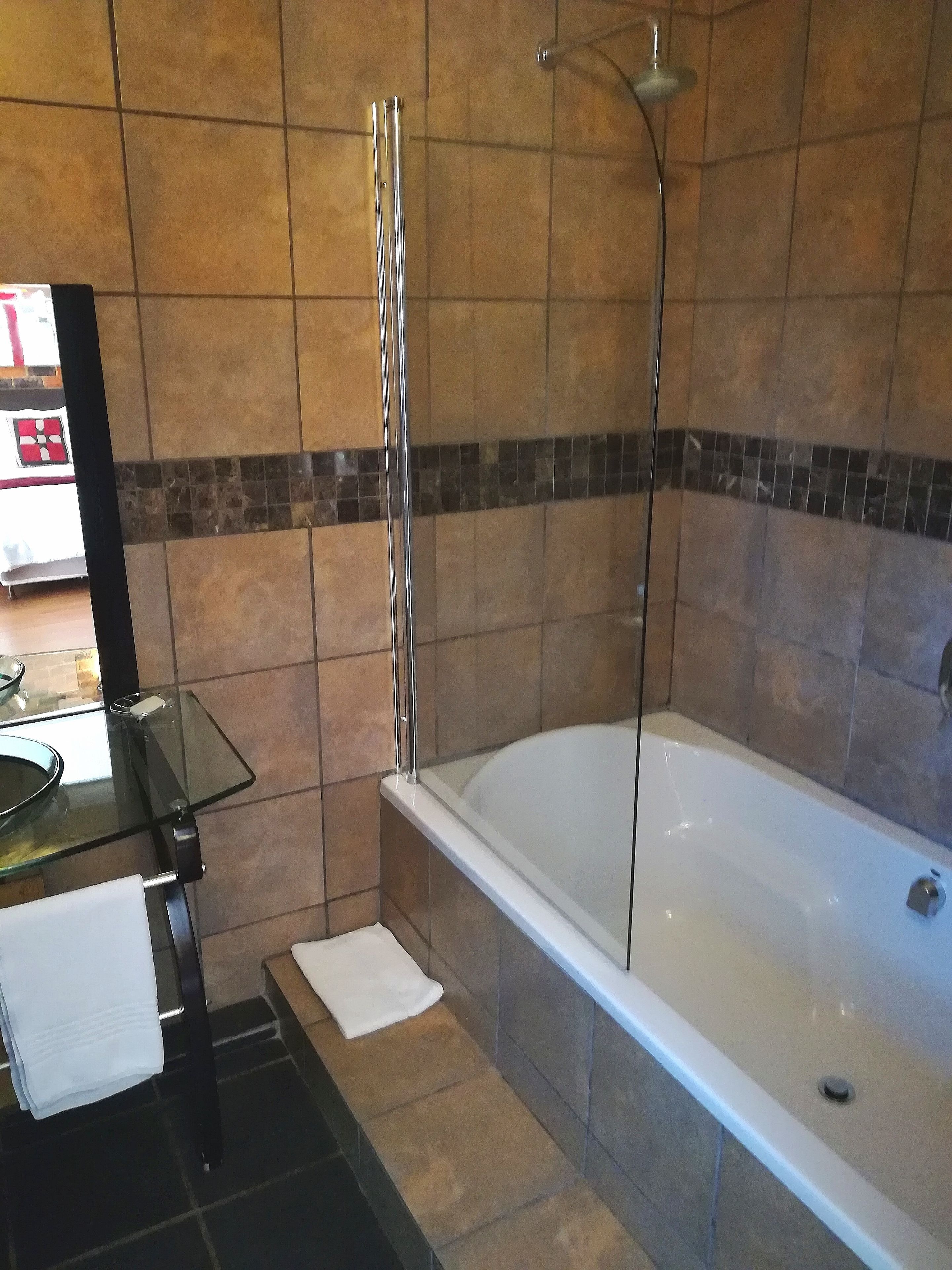 A bathroom with a glass-enclosed shower, a white bathtub, and a glass-topped vanity with a towel.