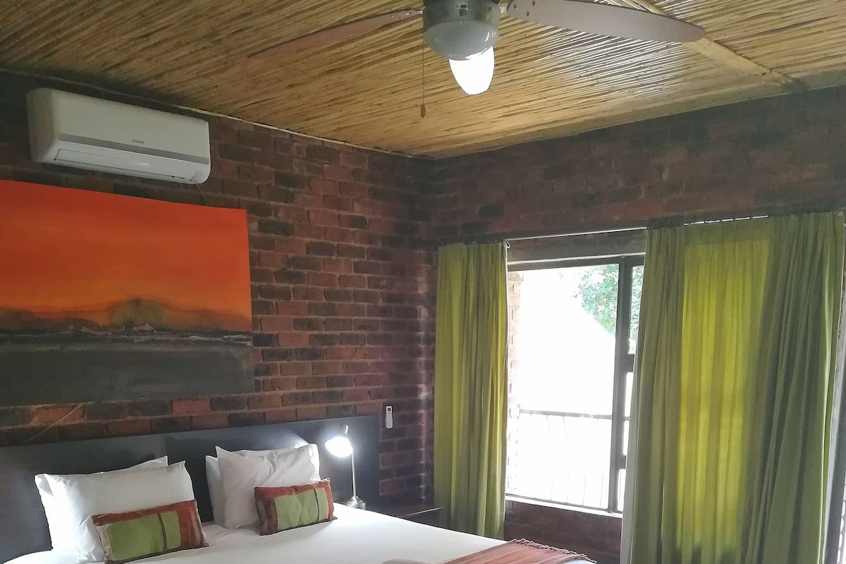 Ein Hotelzimmer mit einem großen Bett, einem Deckenventilator, einer Ziegelwand und einem Fenster mit Vorhängen.