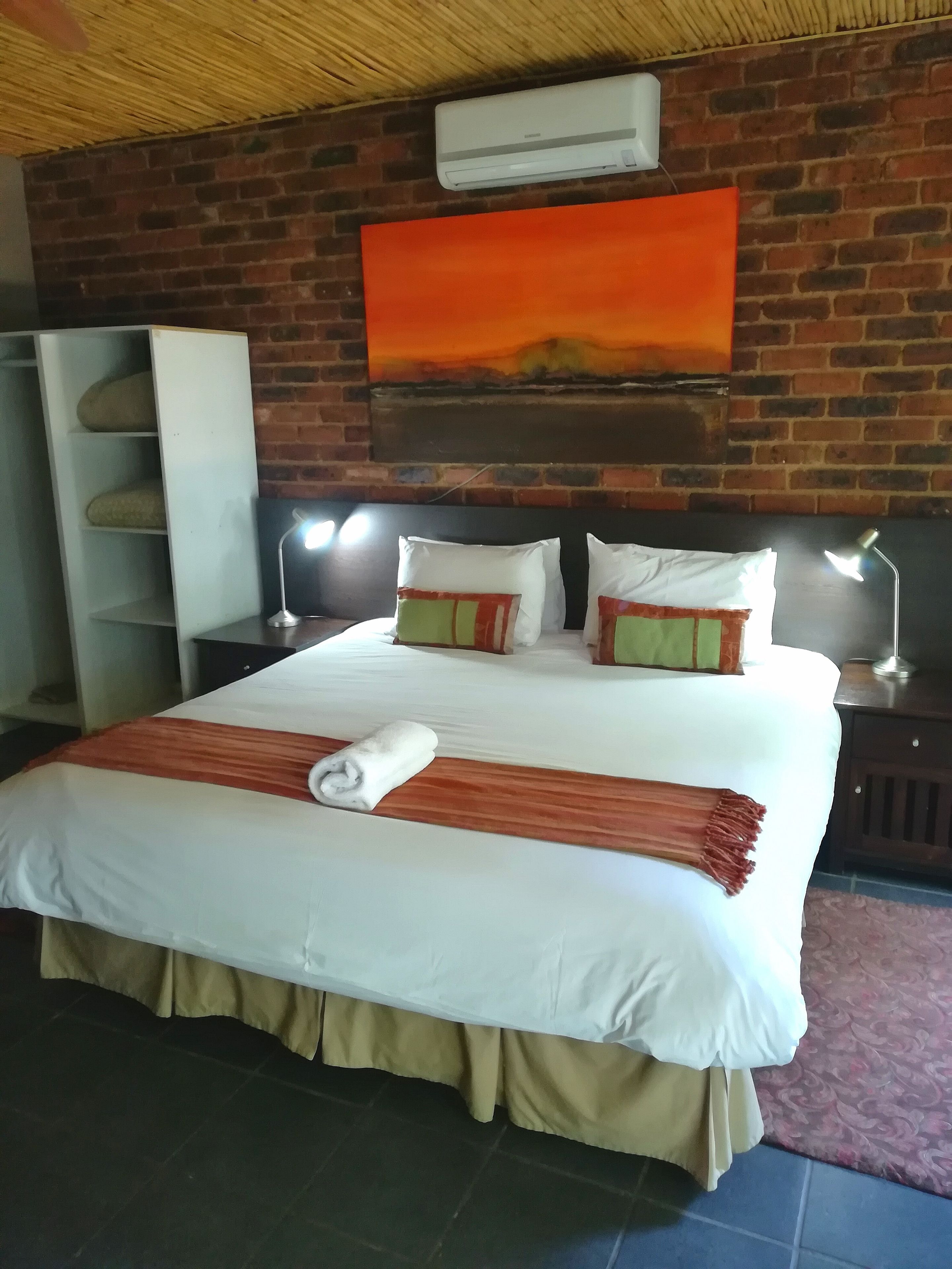 A hotel room with a brick wall, a large bed with white bedding, two bedside lamps, and a red blanket.