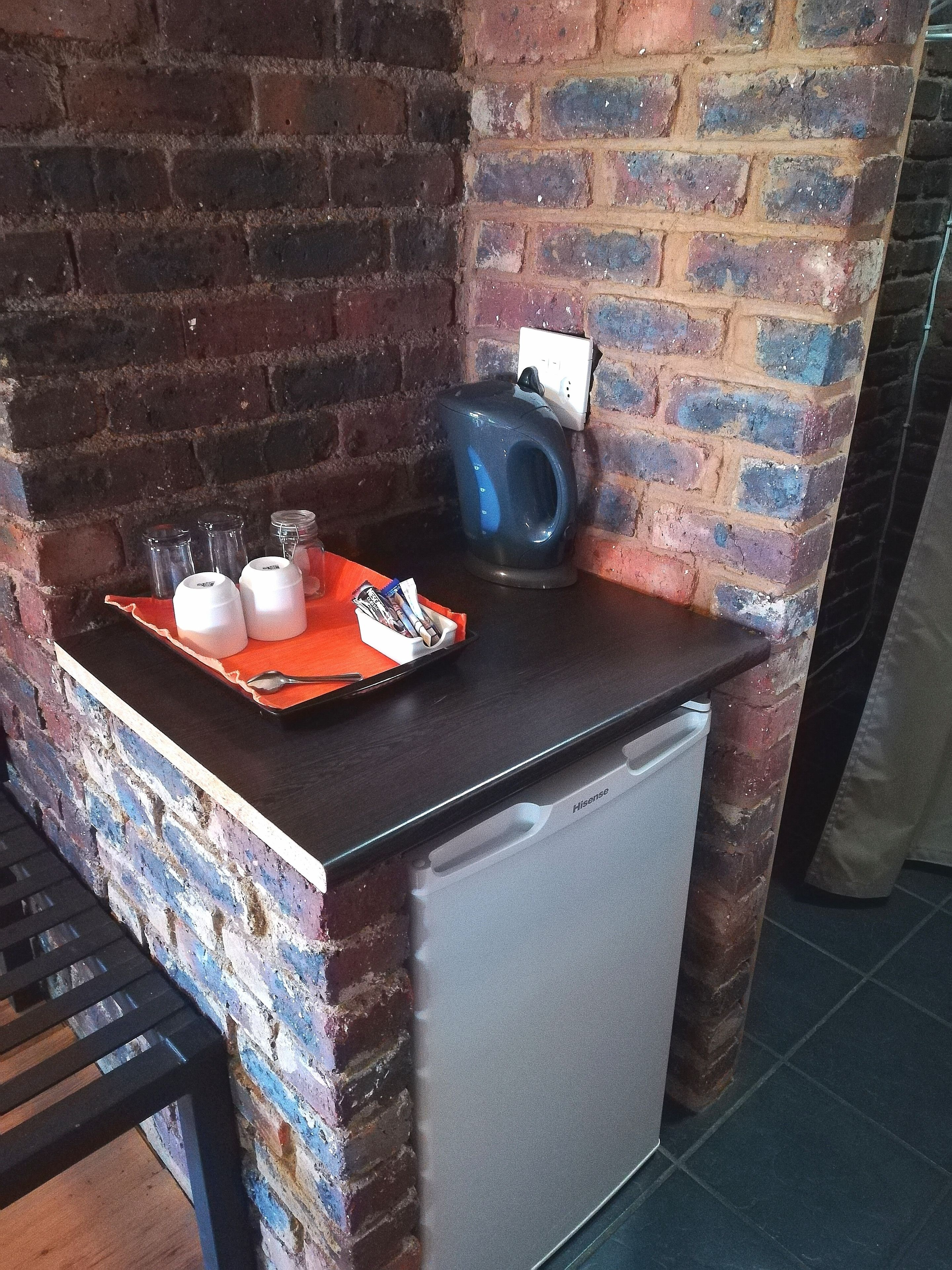 A kitchen area with a brick wall, a small refrigerator, and a tray with cups and a spoon.