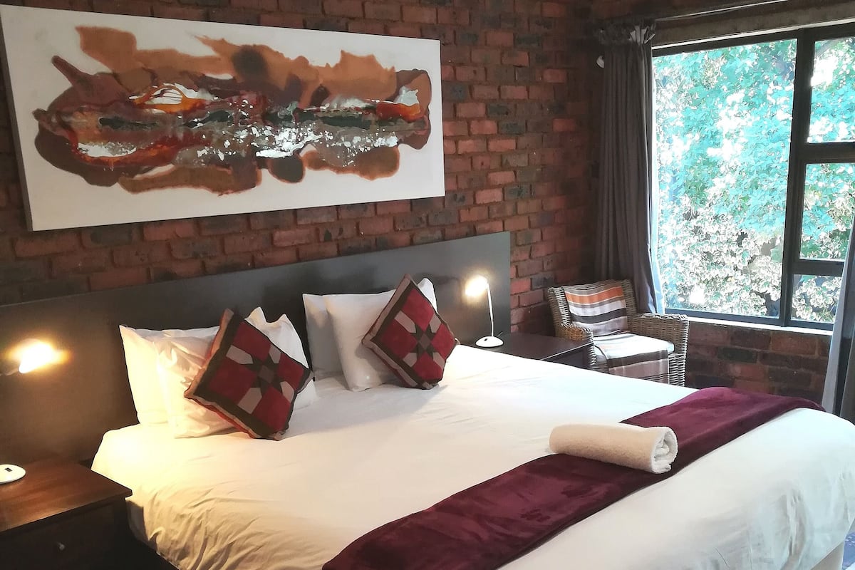 Ein Hotelzimmer mit einem großen Bett, einer Ziegelwand, einem Fenster mit Blick auf Bäume und einem Gemälde über dem Bett.