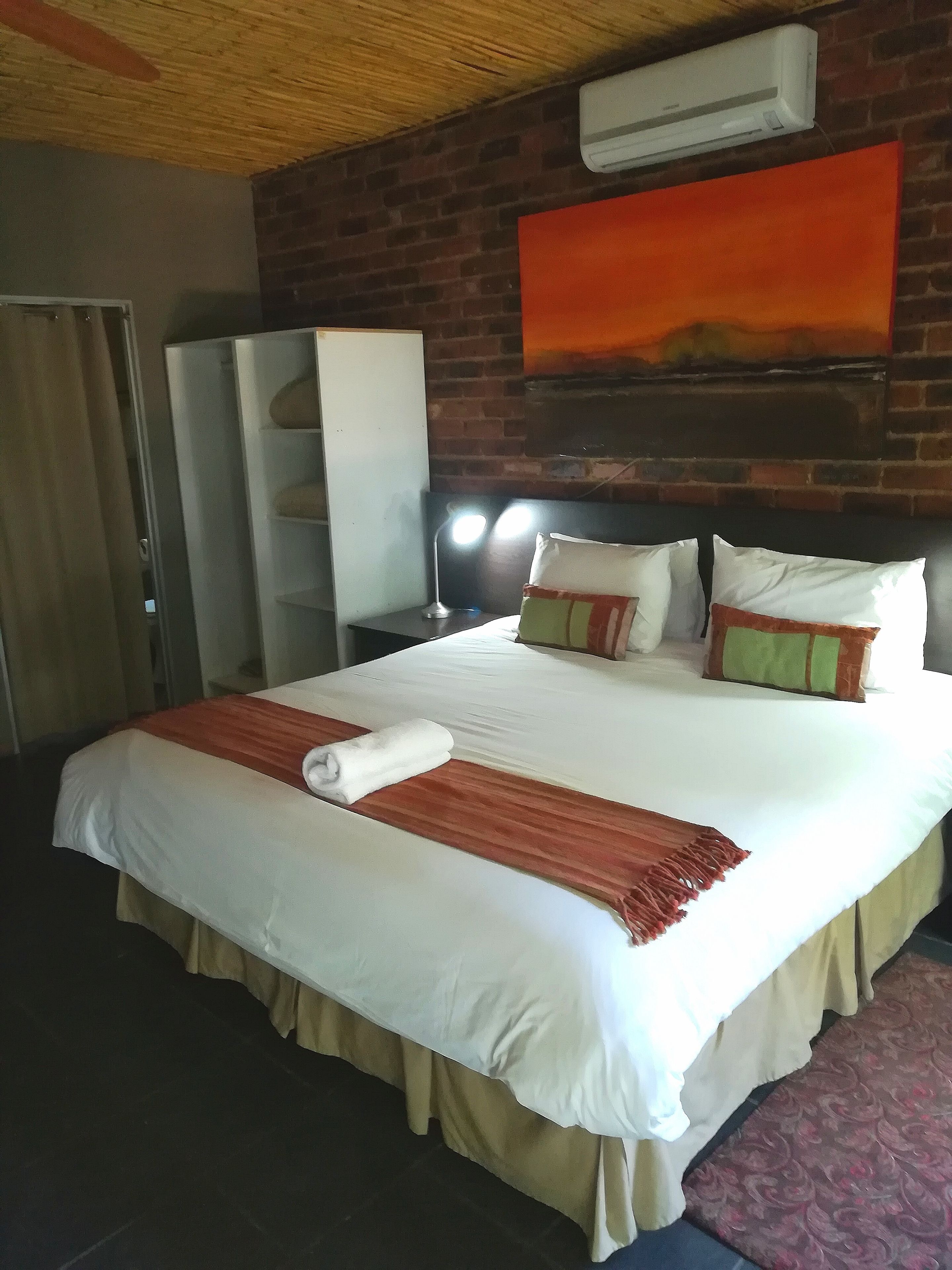 Et hotelværelse med en stor seng, et garderobeskab, et skrivebord med lampe og en aircondition-enhed på væggen.