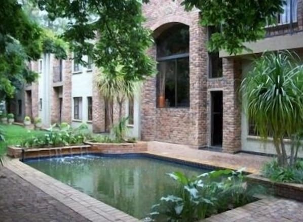 Une cour avec une piscine, entourée de bâtiments en briques et d’une végétation luxuriante.