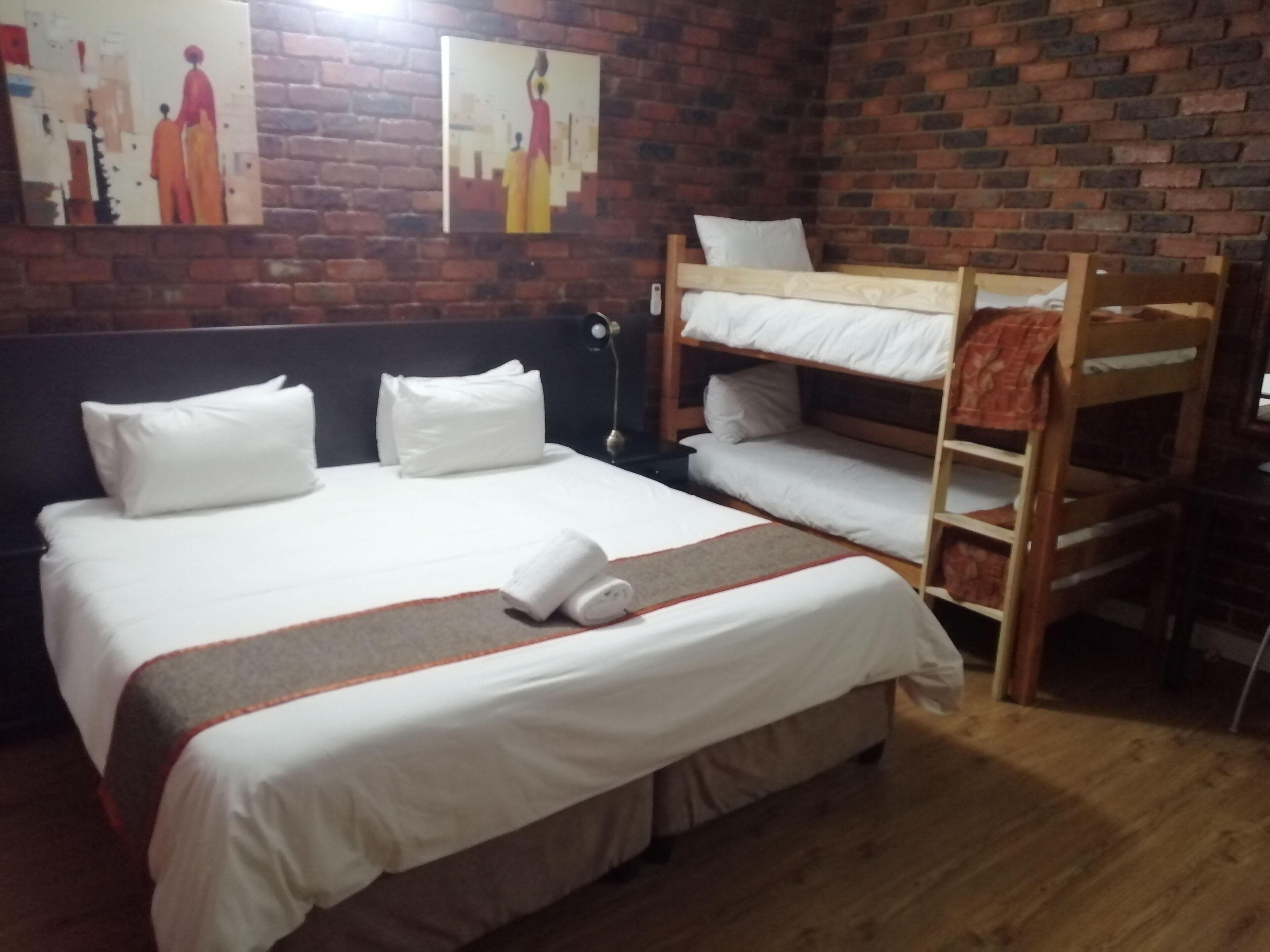 Una habitación de hotel con una cama grande, dos camas literas, una pared de ladrillo y obras de arte en la pared.