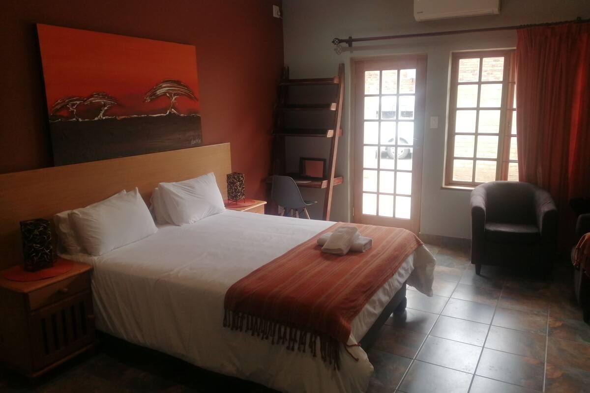 Ein Hotelzimmer mit einem großen Bett, einem Schreibtisch, einem Stuhl und einem Fenster mit Vorhängen.