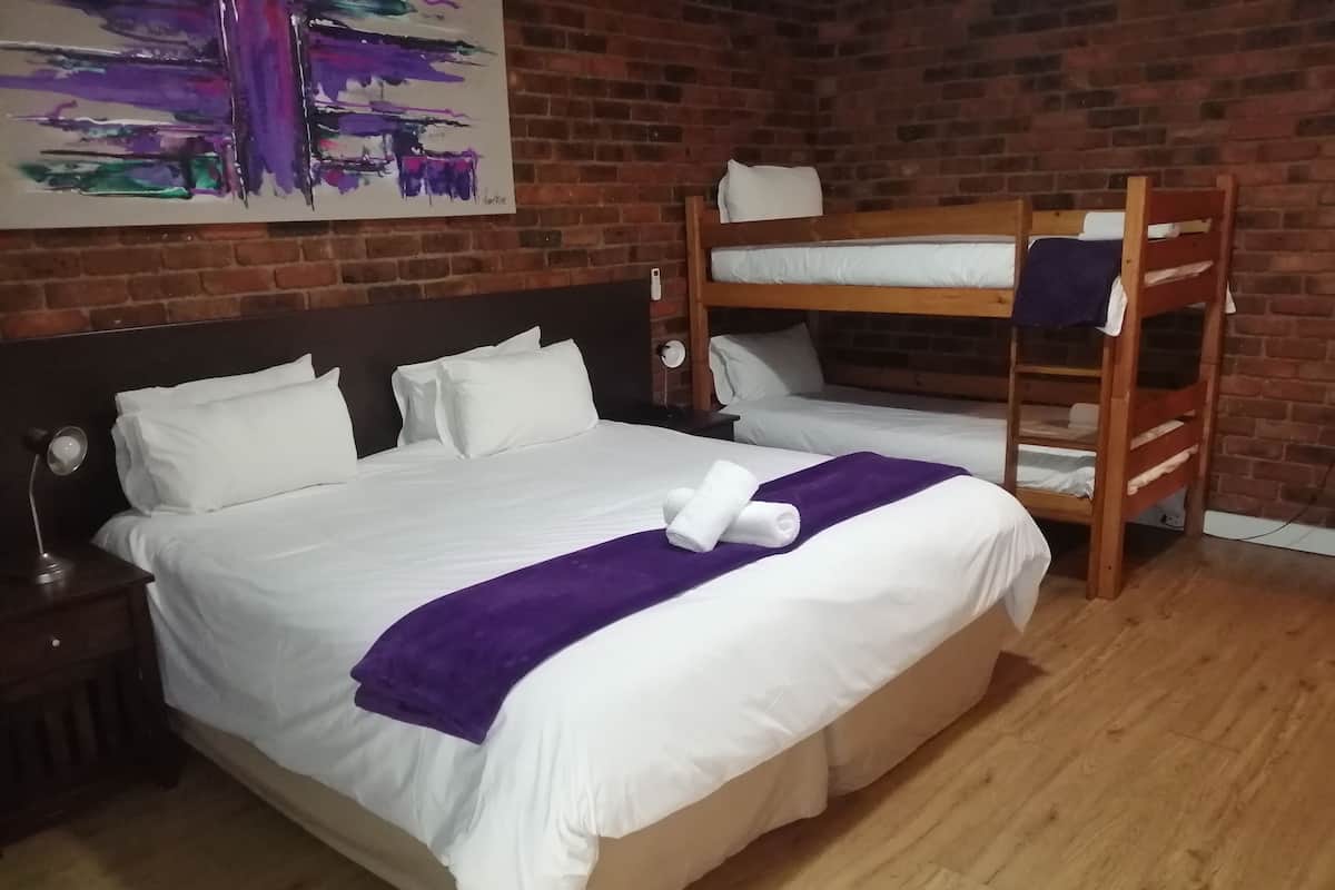 Ein Hotelzimmer mit einem großen Bett, zwei Einzelbetten, einem hölzernen Etagenbett, einer violetten Tagesdecke und einem Bild an der Wand.