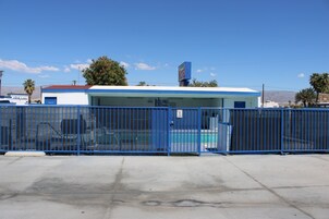 Um motel com fachada azul, área de estacionamento cercada e uma placa indicando que é um motel.