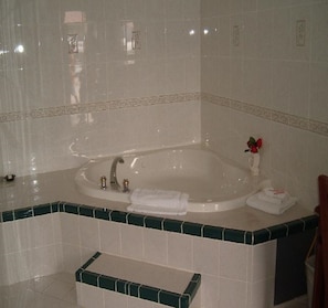 A bathroom with a large bathtub, a sink, and a bench. - City Center Motel (Indio)