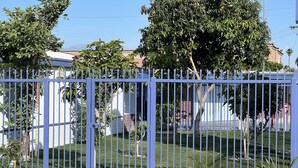 A gated residential area with a clear sky, a white picket fence, and a well-maintained lawn. - City Center Motel (Indio)