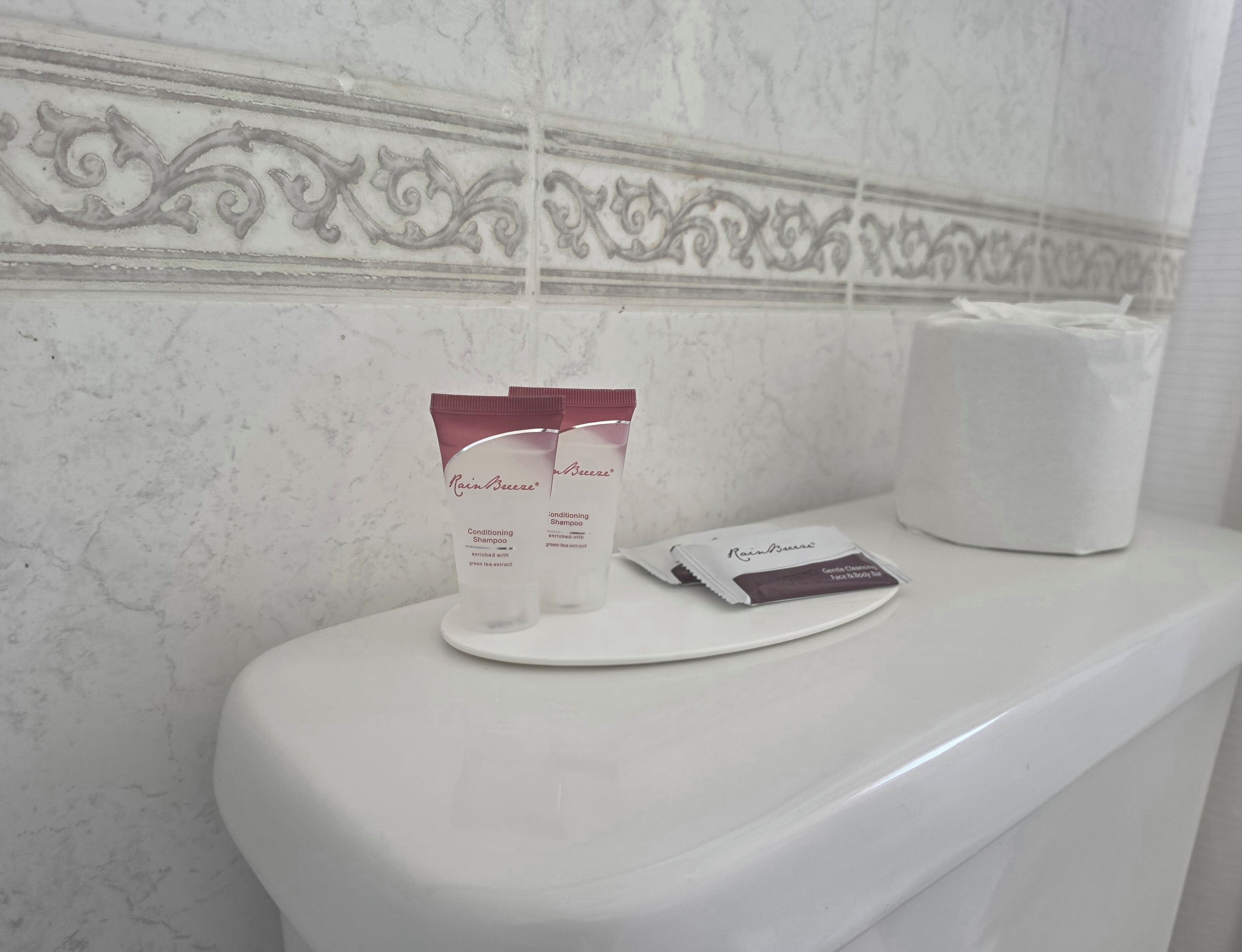 Un baño con pared de mármol, un inodoro blanco y una caja de pañuelos.