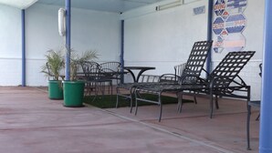 A covered outdoor seating area with metal chairs and tables, potted plants, and a wall with safety signs. - City Center Motel (Indio)