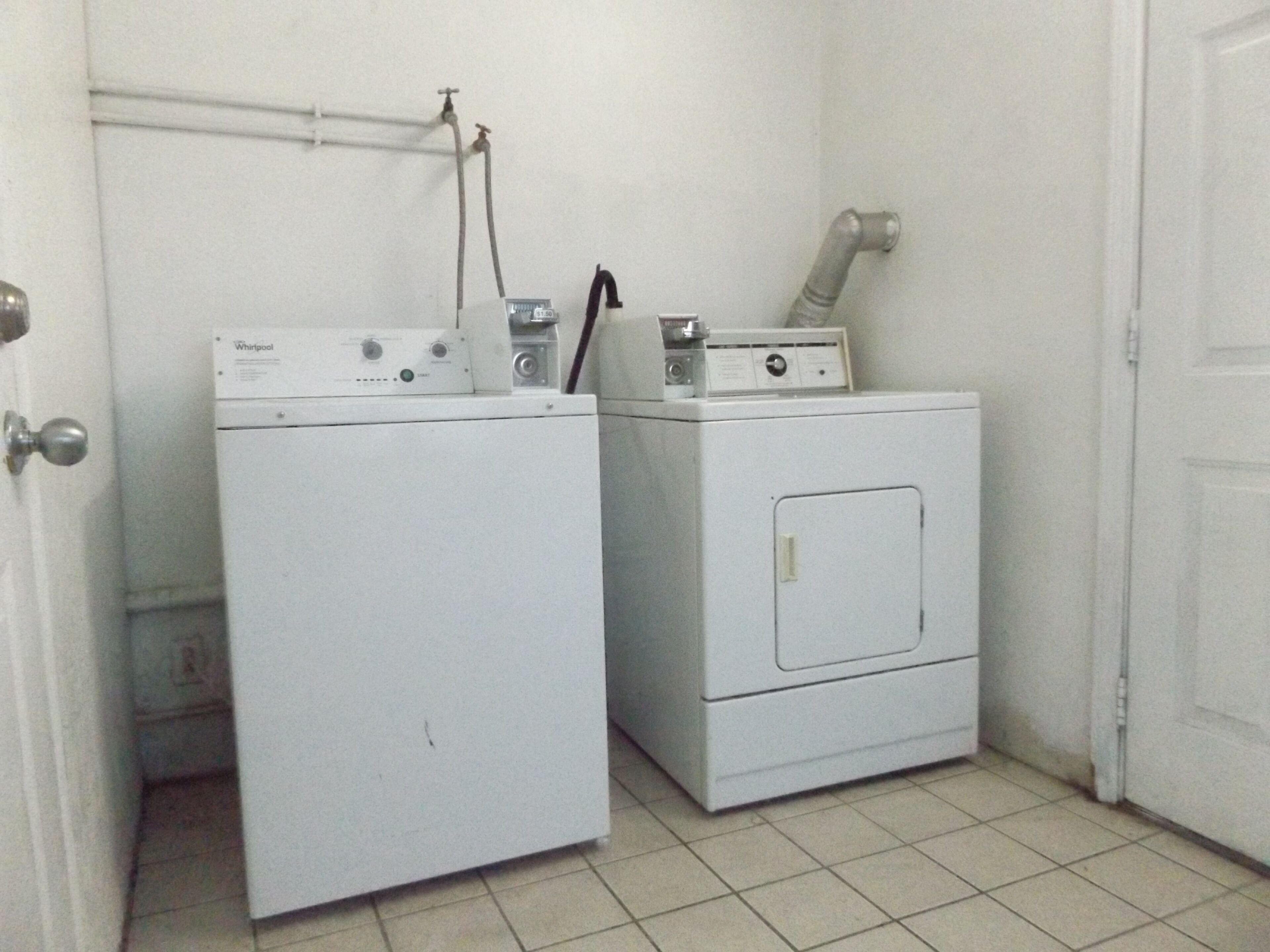 A laundry room with two stacked washers and dryers, a white door, and a tiled floor.