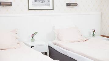 Habitación de hotel con dos camas, paredes blancas, un cuadro enmarcado y un jarrón pequeño con flores.