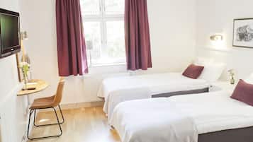 Ett hotellrum med två sängar, ett skrivbord, en stol, en TV och ett fönster med gardiner.